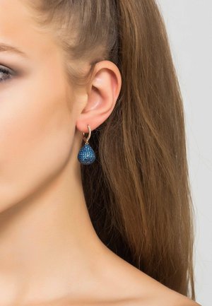 Orecchini a goccia in cristallo blu con forma a goccia, accentuati da un anello tono oro. I cristalli presentano dettagli intricati e brillano.