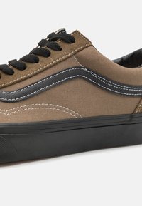 Basket basse marron et noire avec lacets noirs, coutures blanches et semelle en caoutchouc noire.