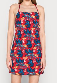 Vestido floral rojo con patrones tropicales en azul y naranja, tirantes finos, corpiño ajustado y falda acampanada, hecho de tela ligera.