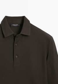 Ciemnozielona koszulka polo o teksturowanej powierzchni, z płaskim kołnierzem, trzema guzikami przy rozporku oraz metką marki wewnątrz kołnierzyka.