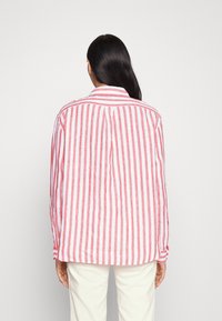 Camisa de rayas rojas y blancas en tejido ligero, con cuello, puños abotonados y un corte relajado. Costuras visibles y ligera textura.