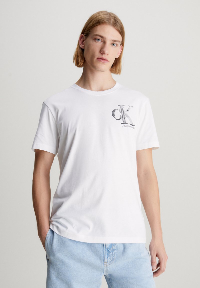 Balta medvilninė t-shirt su apykakle ir trumpomis rankovėmis. Papuošta juodu „CK“ logotipu ir „Calvin Klein Jeans“ tekstu ant krūtinės.