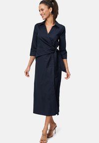Navy wrap dress with long sleeves and a waist tie, made of smooth fabric. Features a collar and a full-length design.
