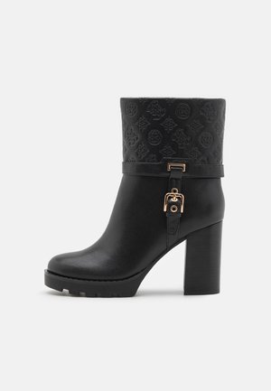 Bottine en cuir noir avec manchette à motif embossé, sangle à boucle dorée, talon bloc et semelle crantée, vue de côté sur fond blanc.