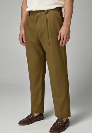 Brown pleated trousers with a straight leg design, crafted from lightweight fabric. Worn with dark loafers.