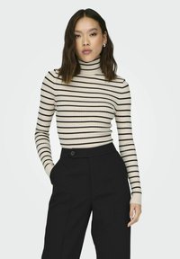 Striped turtleneck sweater in cream with black stripes, ribbed texture. Paired with high-waisted black trousers featuring a button detail.