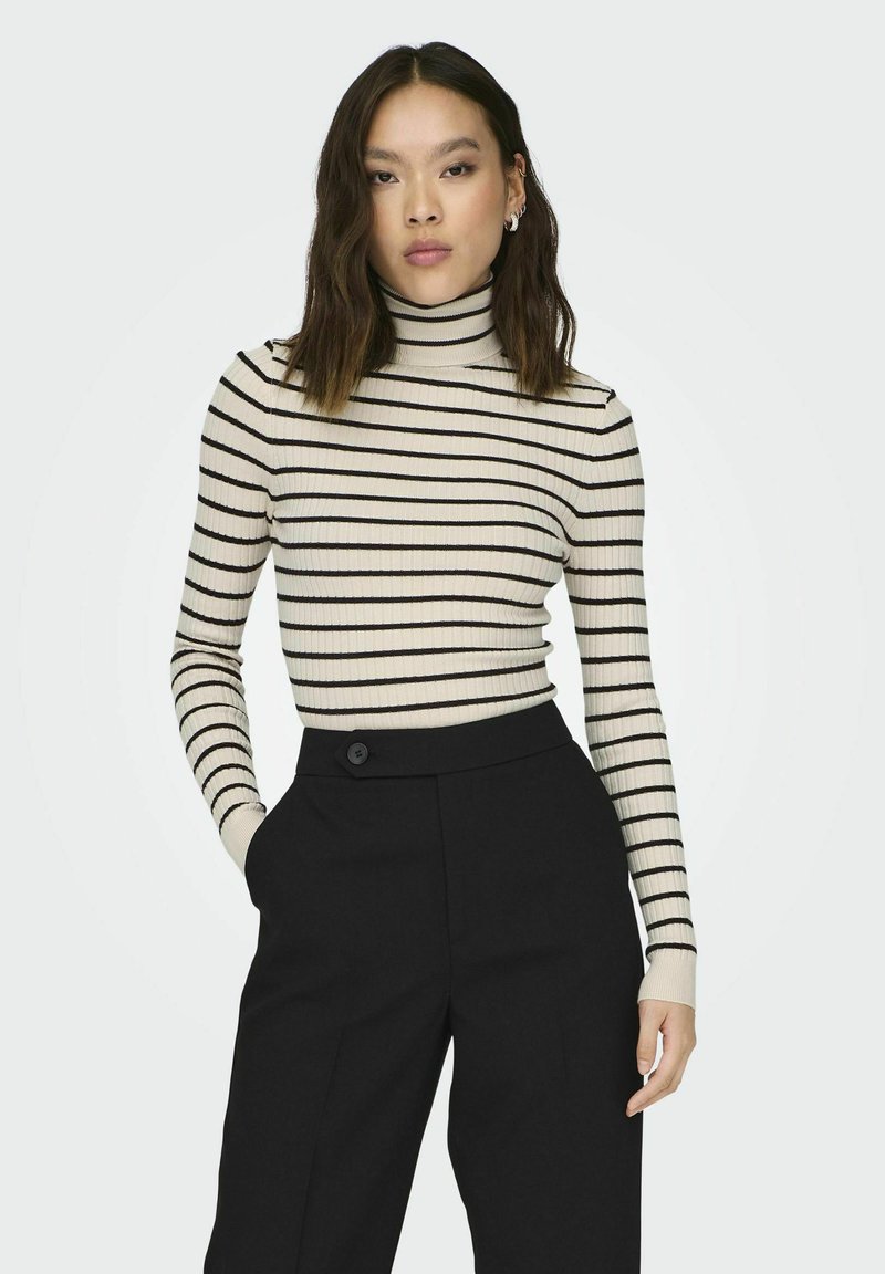 Striped turtleneck sweater in cream with black stripes, ribbed texture. Paired with high-waisted black trousers featuring a button detail.