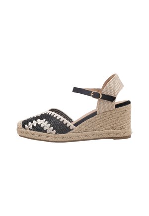 Sandalia de cuña con tacón beige tejido, punta tejida en blanco y negro, y correa negra en el tobillo con hebilla dorada, vista lateral sobre fondo blanco.