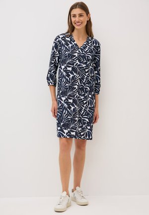 Navy blue dress with white leaf patterns, V-neck, and three-quarter sleeves. Worn with white sneakers. Cotton blend fabric, knee-length.