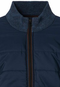 Marineblaue Steppjacke mit hohem, geripptem Kragen aus strukturiertem marineblauem Strick und einem braunen Reißverschluss, mit horizontalen Steppnähten.