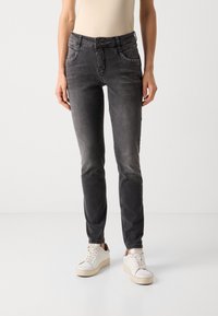 Slim fit, sötétszürke farmernadrág elülső zsebekkel, díszes szegecsekkel a zseb szélein és klasszikus gombzárással, fehér sportcipővel párosítva.