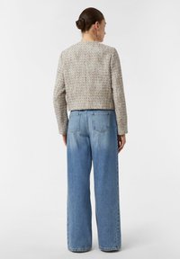 Teksturowany, skrócony beżowy sweter z okrągłym dekoltem, noszony z luźnymi, jasnoniebieskimi dżinsami. Styl casualowy, widok z tyłu.