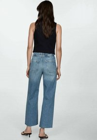 Jeans de mezclilla azul claro de talle alto y pierna ancha, con dos bolsillos traseros y un acabado sutilmente desteñido. Combinados con un top negro sin mangas.