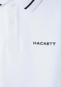 Biała koszulka polo z fakturowanego materiału, z czarnym wykończeniem kołnierzyka oraz haftowanym na czarno logo "HACKETT".