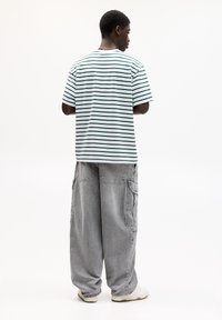 Tricou cu mânecă scurtă, în dungi, alb cu dungi verzi, purtat cu pantaloni cargo gri, largi și adidași albi.