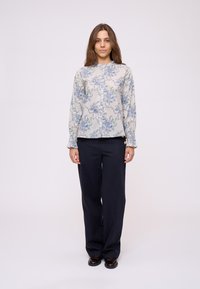 Blusa floreale azzurro chiaro con maniche lunghe, colletto e chiusura a bottoni, abbinata a pantaloni larghi blu navy e scarpe scure.