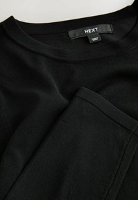 Sort strikket crewneck-trøje med ribkant ved hals og bund, der har en glat tekstur. Etiket "NEXT" synlig på indersiden.