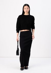 Μαύρο ribbed crop πουλόβερ συνδυασμένο με εφαρμοστό μαύρο maxi φούστα. Το σύνολο διαθέτει λείο ύφασμα και μινιμαλιστικό σχεδιασμό, συμπληρωμένο από μια μικρή μαύρη τσάντα.