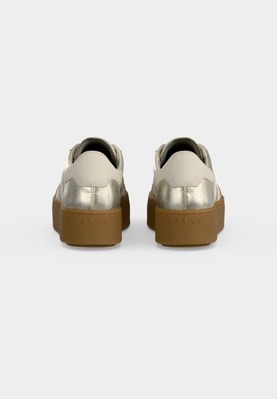 Paire de baskets blanches et argent métallisé avec des semelles épaisses marron montrée de dos sur un fond clair uni.