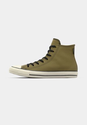 Adidași înalți de culoare verde măslin cu șireturi negre, vârf de cauciuc și talpă albă, având un finisaj texturat și accente contrastante negre.