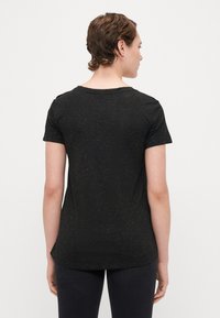 Sort kortærmet T-shirt med rund halsudskæring og en struktureret overflade, der har diskrete guldpletter spredt over stoffet.