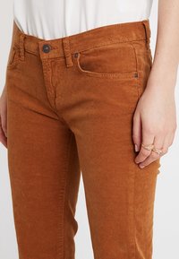 Corduroy broek in roestoranje met een getailleerd ontwerp, voorzien van vijf zakken, een knoopsluiting en een subtiele ribbelstructuur.