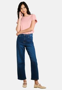 T-shirt rosa a maniche corte, jeans blu a gamba larga e ballerine beige chiaro. Design semplice, texture morbida e vestibilità casual.