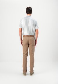 Košile s krátkým rukávem, světle modro-bílé pruhované, v kombinaci s béžovými kalhotami. Oblečení doplňuje hnědý opasek a zelenkavé boty.