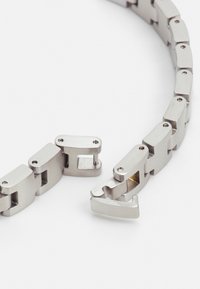 Bracelet en acier inoxydable avec des maillons entrelacés, doté d'une finition brossée et d'un fermoir sécurisé. Formes rectangulaires lisses avec de petites vis.