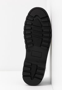 Semelle en caoutchouc noir avec des motifs de bande de roulement profonds, surface texturée, talon oval et marque de taille. Design optimisé pour l'adhérence et la durabilité.