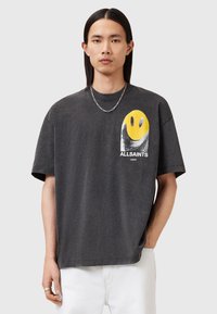 Grå oversized t-shirt lavet af bomuld med et gult smiley-tryk og sorte detaljer, der har korte ærmer og en afslappet pasform.