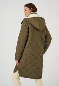 Abrigo acolchado verde oliva con capucha, que cuenta con un cuello en color crema. De longitud media con aberturas laterales, confeccionado en tela suave y mate.