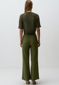 Top court en tricot vert à manches courtes associé à un pantalon large taille haute vert olive. Texture lisse et silhouette ajustée.