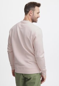 Felpa rosa chiaro con maniche lunghe e polsini a costine, caratterizzata da un collo rotondo e una texture liscia, abbinata a pantaloni verde oliva.
