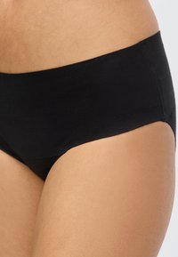 Κοντινό πλάνο ενός ατόμου που φοράει μαύρα seamless εσώρουχα τύπου hipster με ομοιόμορφο ύφασμα και χωρίς ορατές ραφές.