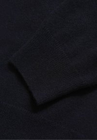 Gros plan sur une manche de pull tricoté bleu marine foncé avec détail en côte au niveau du poignet.