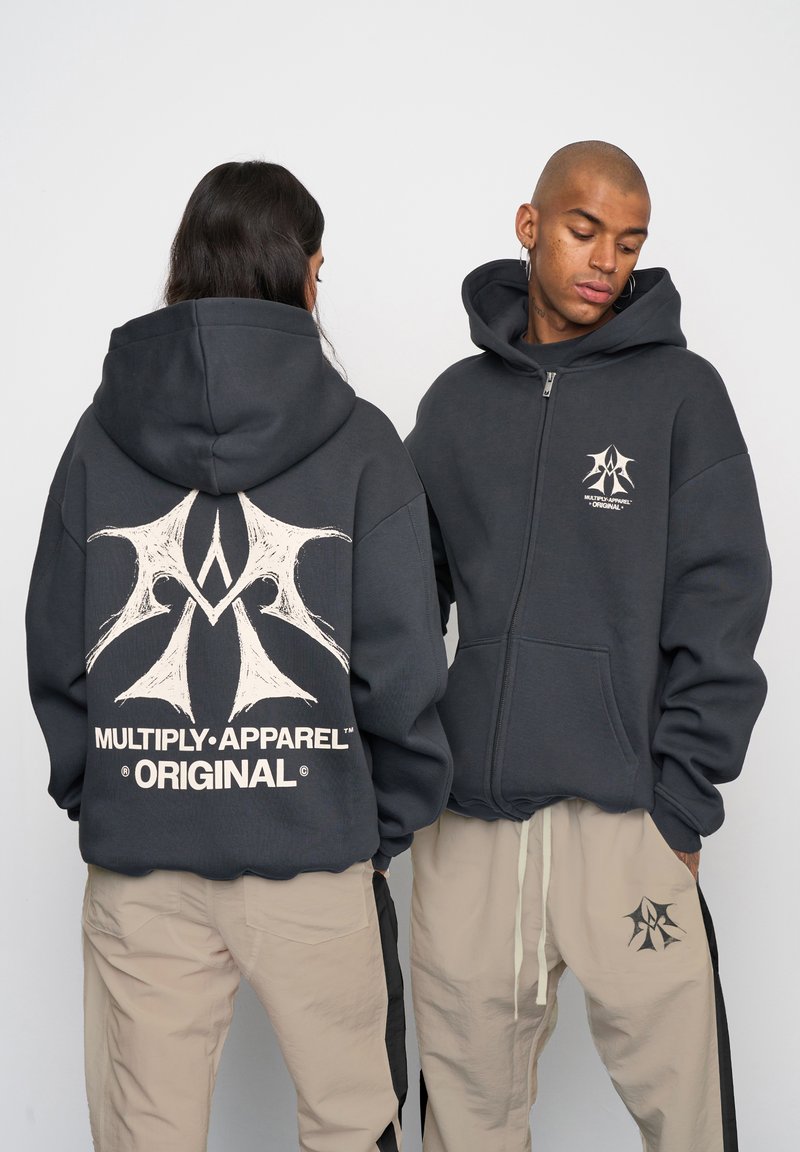 Tmavošedá mikina s kapucňou na zips a bielym grafickým logom na chrbte a hrudi. Obsahuje veľkú kapsu a sťahovaciu kapucňu. Predvedená na dvoch modeloch.