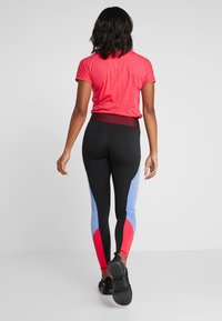 Top corto rojo de manga corta combinado con leggings en bloques de color negro, azul claro y rojo. Los leggings tienen un diseño ajustado y una cintura alta.