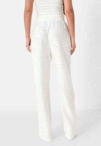 Witte broek met een gestructureerd golfpatroon, relaxed fit en een elastische tailleband. De stof lijkt lichtgewicht en zacht, geschikt voor casual draag.