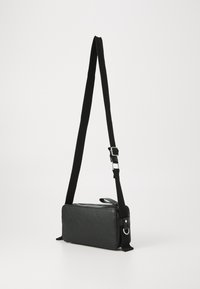 Black crossbody bag made of smooth synthetic material with a rectangular shape. Features an adjustable strap and zip closure.