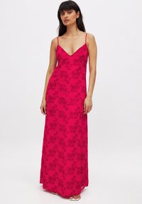 Robe maxi fuchsia avec fines bretelles, décolleté en V profond et broderie florale noire. La robe a une texture lisse et une silhouette ajustée.