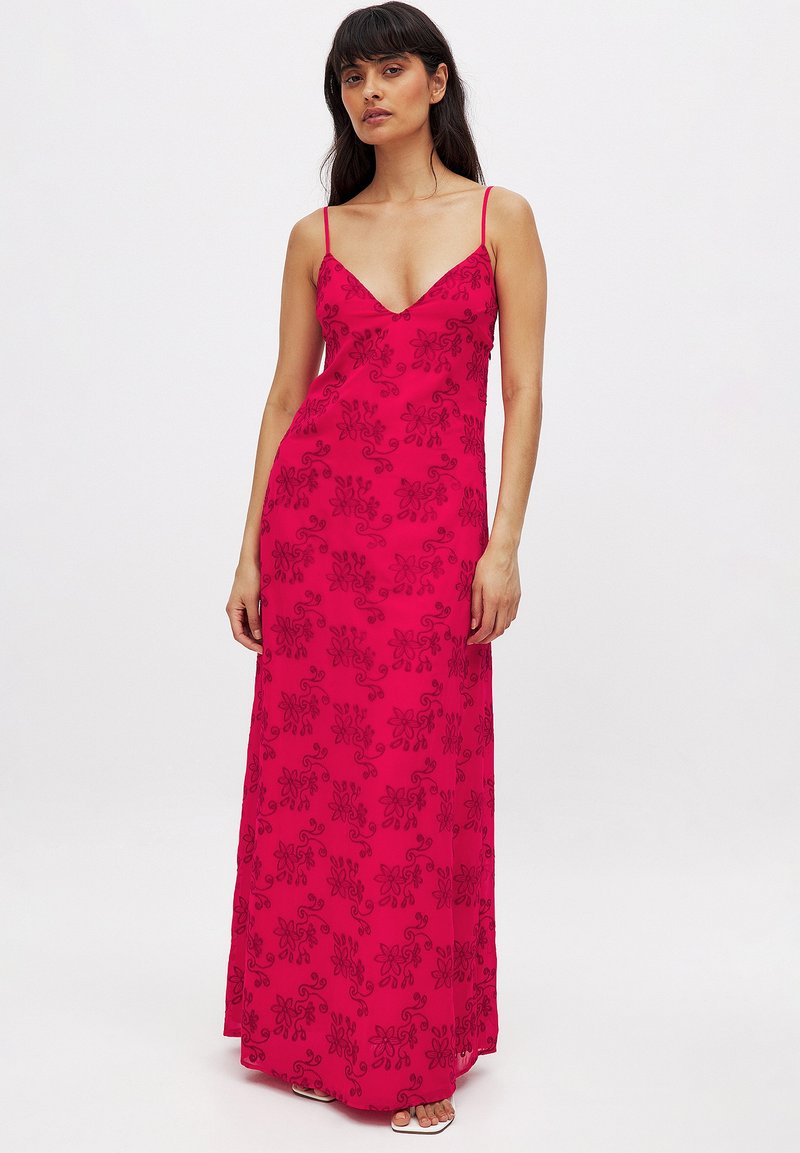 Robe maxi fuchsia avec fines bretelles, décolleté en V profond et broderie florale noire. La robe a une texture lisse et une silhouette ajustée.