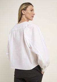 Weiße Bluse mit langen Ärmeln, puffartigen Ärmeln, rundem Ausschnitt und lockerer Passform. Weicher Baumwollstoff mit einfachem Design.