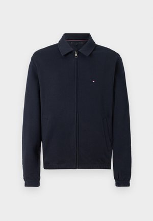 Marinblå zipjacka med krage, elastiska ärmslut och sidofickor. Har en liten logotypdetalj på vänster bröst.