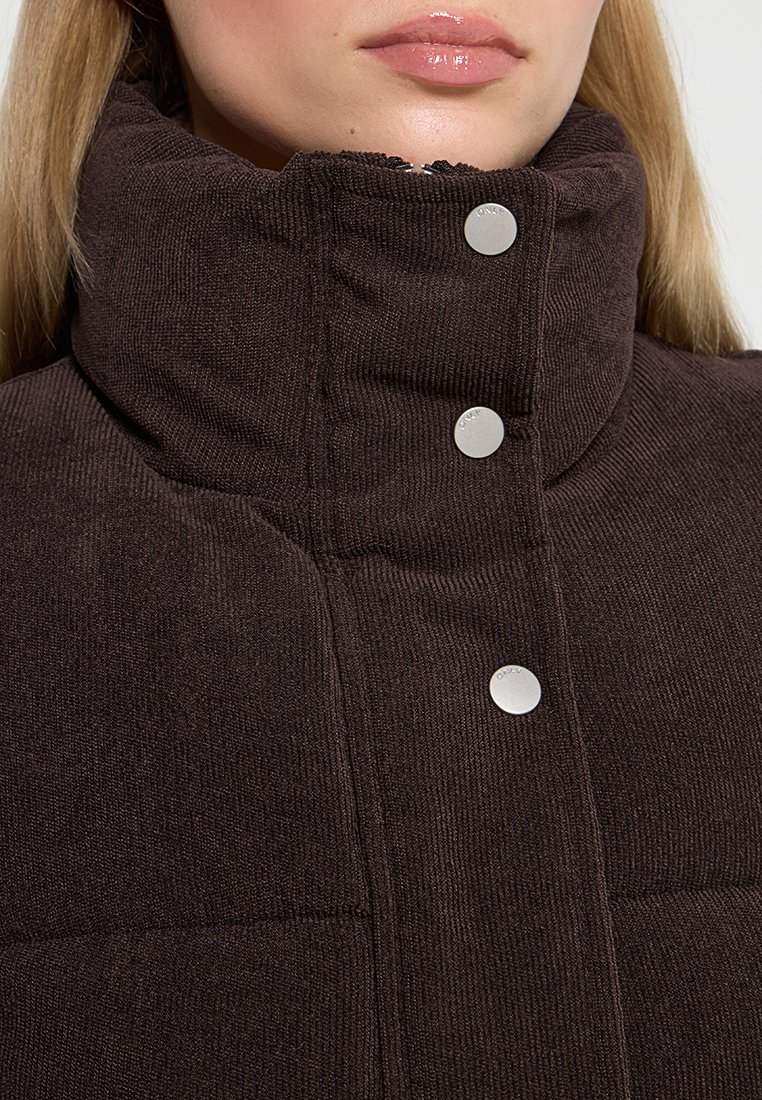 Braune Corduroy-Pufferjacke mit hohem Kragen, ausgestattet mit silbernen Druckknöpfen und gesteppten Texturdetails.