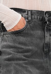 Gonna in denim nero con vita alta, tasca frontale e una leggera trama scolorita. Include chiusura con bottone in metallo e zip.