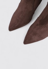Bottines en daim marron avec un design à bout pointu. La texture est douce et la surface apparaît lisse avec un minimum de détails.