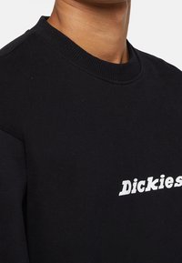 Černá mikina s žebrovaným výstřihem a bílým logem potištěným na hrudi, vyrobená z měkké směsi bavlny.