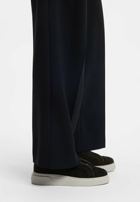 Czarne, szerokie spodnie o luźnych nogawkach, zestawione z ciemnymi, zamszowymi trampkami z białą gumową podeszwą i minimalistycznym wzornictwem.