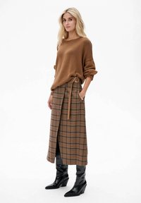 Bruine gebreide trui, geruite wikkelrok in bruin, beige en marineblauw met riem. Zwart kniehoog hakken compleet de outfit.